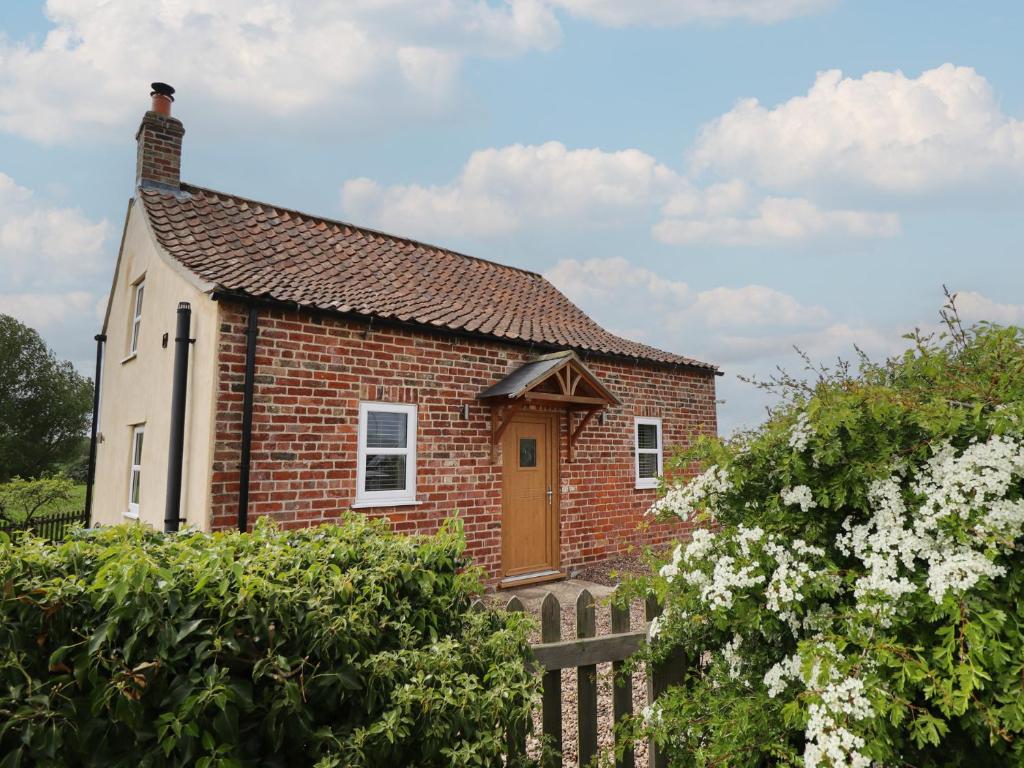 a small brick house with a wooden fence at Shepherd's Cottage in Alford