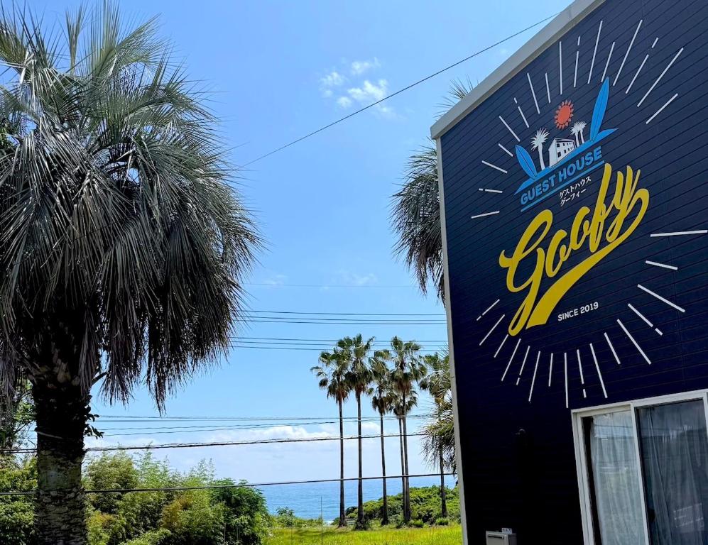 a sign on the side of a building with palm trees at Guest House Goofy in Hyuga