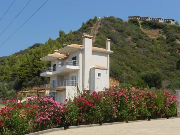 a white house with flowers in front of a hill at Into The Blue in Agia Paraskevi