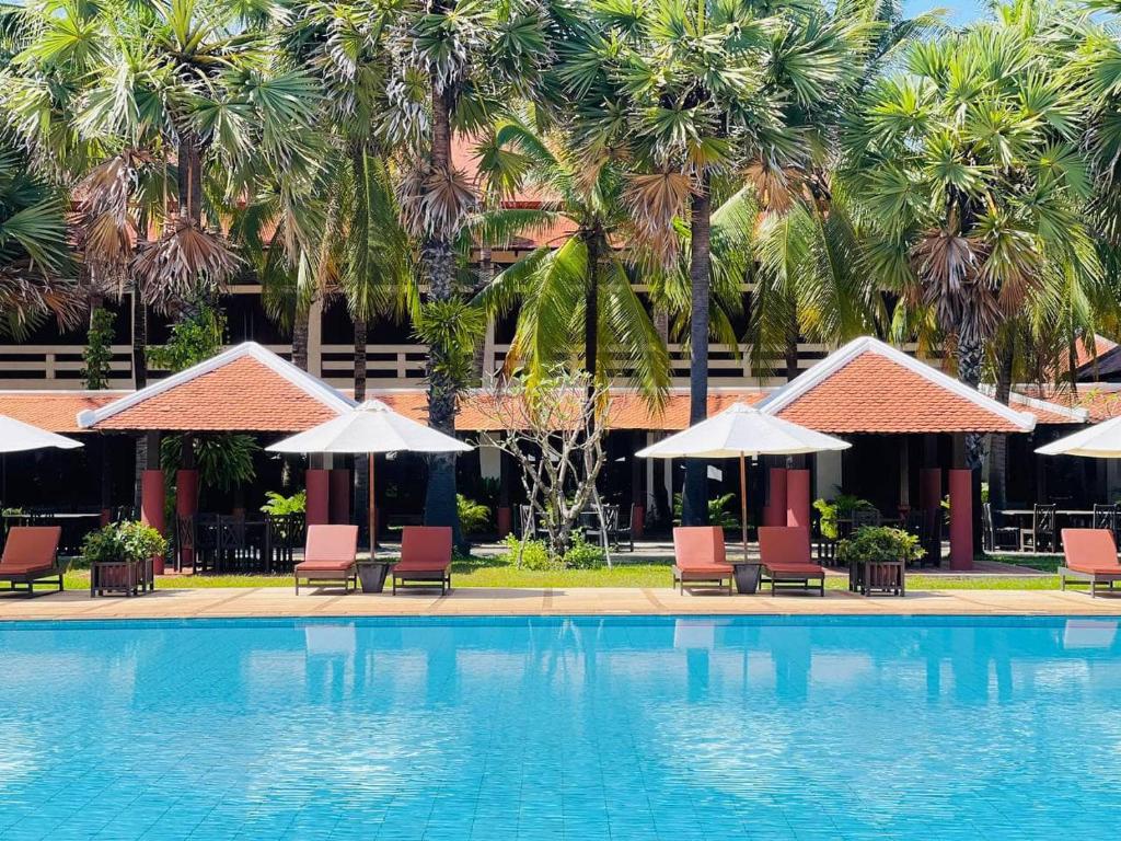 a swimming pool with chairs and umbrellas and palm trees at Royal Angkor Resort & Spa in Siem Reap