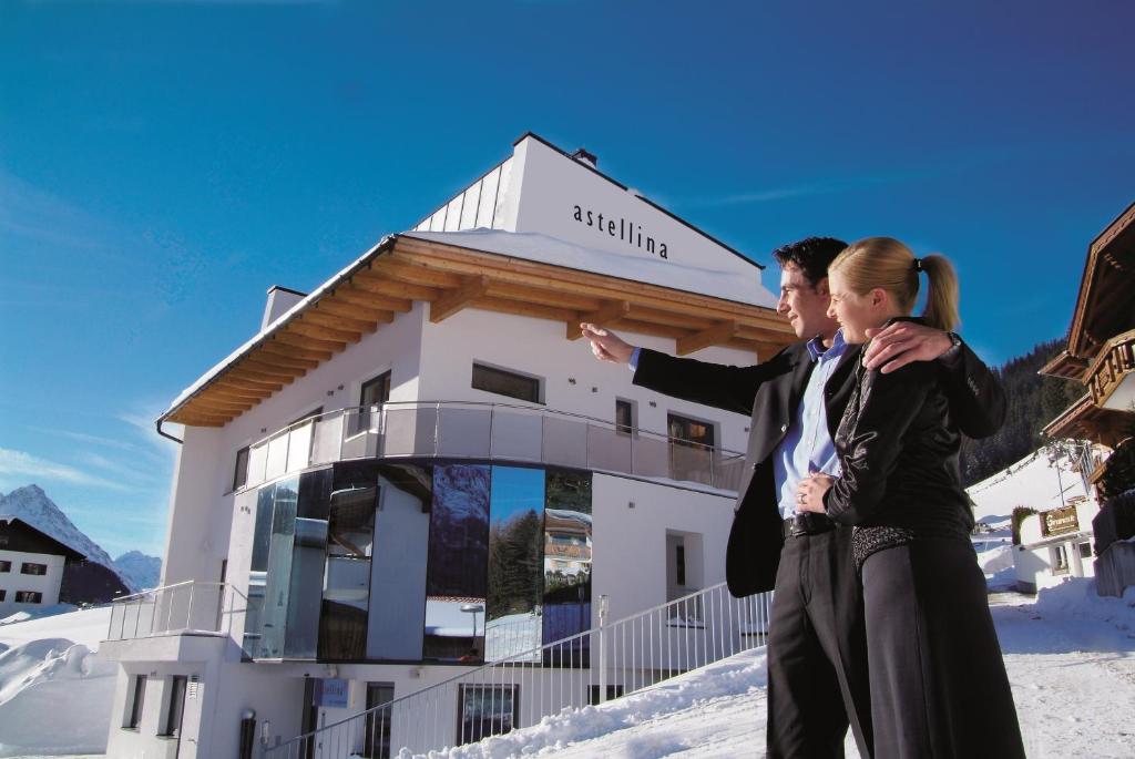 Un uomo e una donna in piedi sulla neve di fronte a un edificio di Astellina hotel-apart a Ischgl