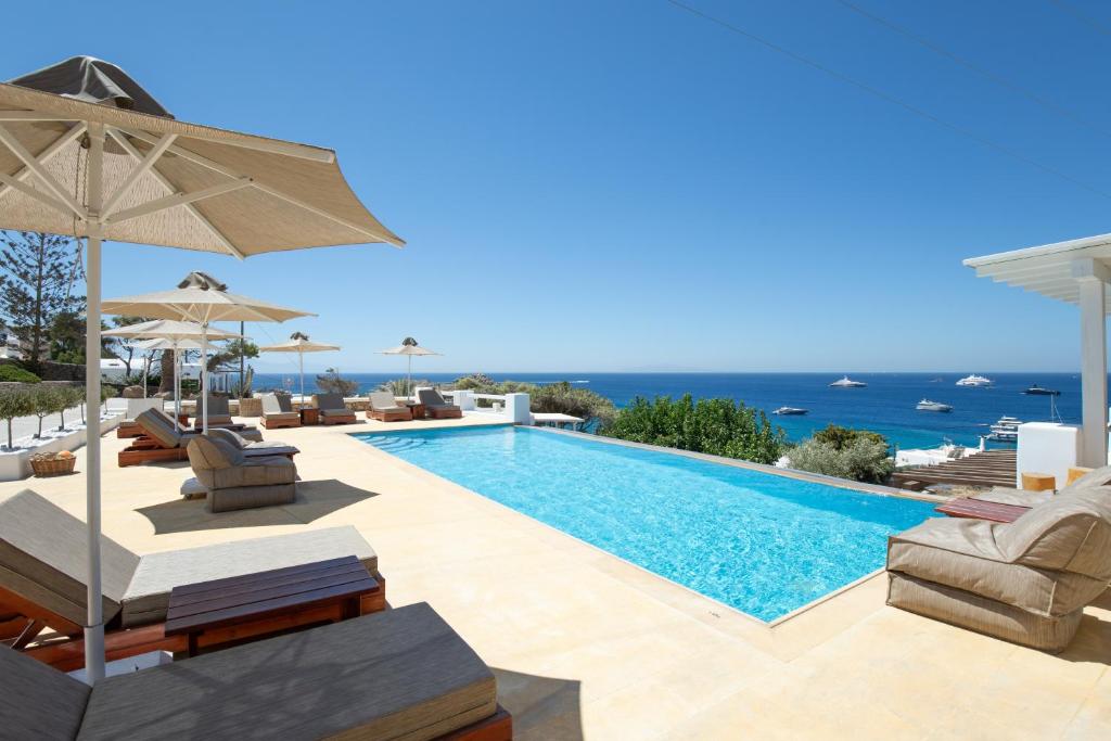 a swimming pool with chairs and an umbrella and the ocean at Seethrough Mykonos Suites in Platis Gialos