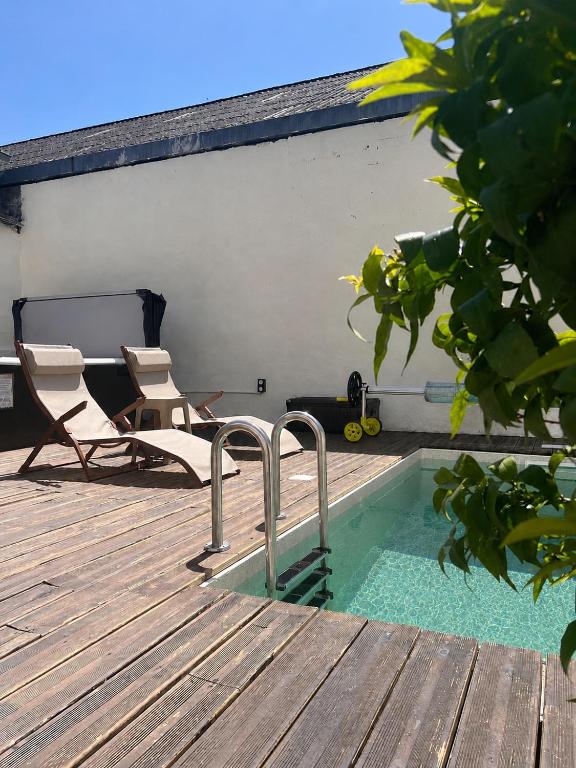 a swimming pool on a deck with two chairs and a table at Maisons Sauvages - Piscine & Jacuzzi - Proche Zoo de Beauval & Châteaux in Romorantin