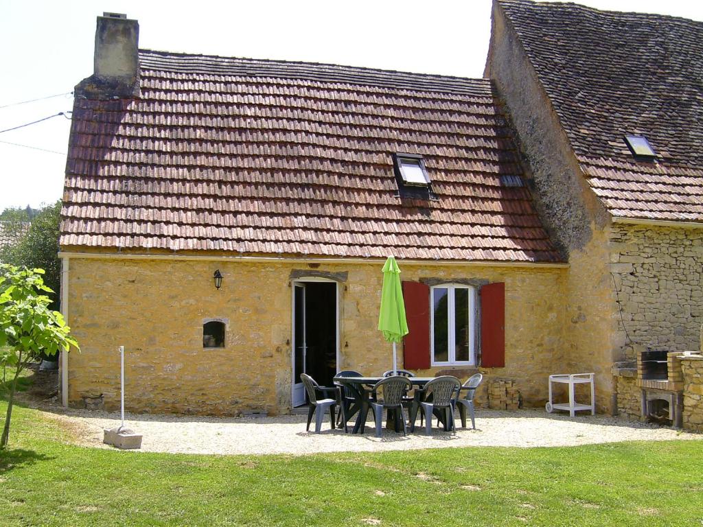 uma casa com uma mesa e cadeiras e um guarda-sol verde em La Prairie em Siorac-en-Périgord