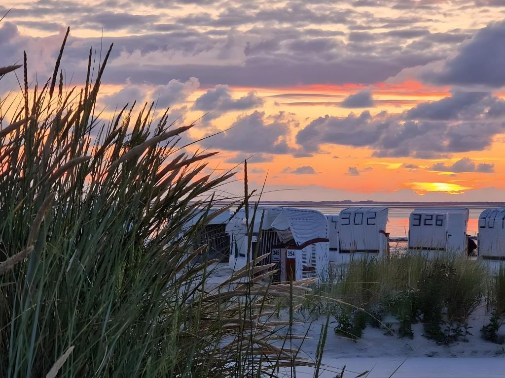 a sunset on the beach with buildings in the sand at Haus am Deich in Norden