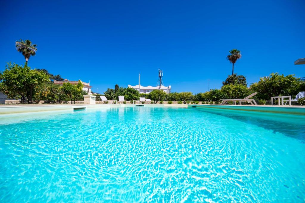 a pool of blue water with palm trees in the background at Villa Fontane Bianche in Fontane Bianche
