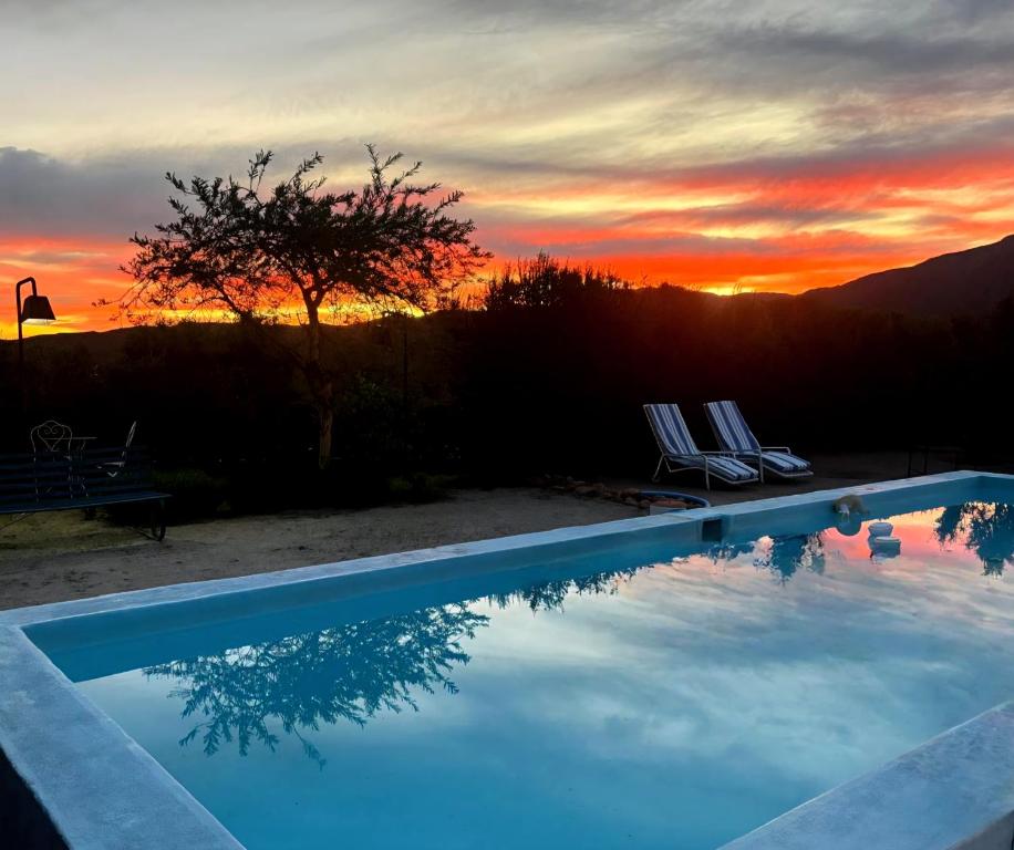 a swimming pool with a sunset in the background at Le Petit Karoo in Oudtshoorn