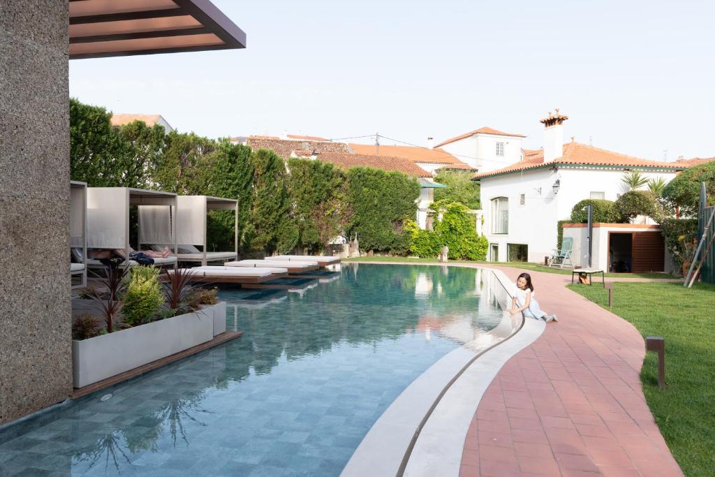 a woman in a white dress is standing next to a swimming pool at Hotel Casa da Nora in Leiria