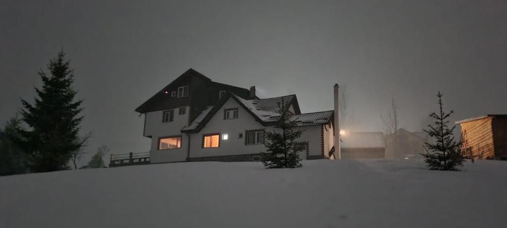 a large house in the snow with lights on at Casa Cătălin-Puntea Craiului in Şirnea
