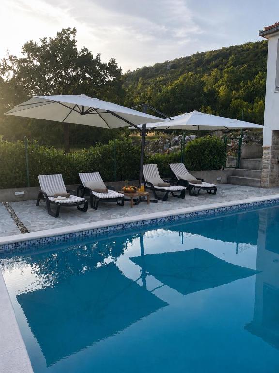 a swimming pool with chairs and umbrellas and a table at Nany-Villa with heated pool in Trolokve