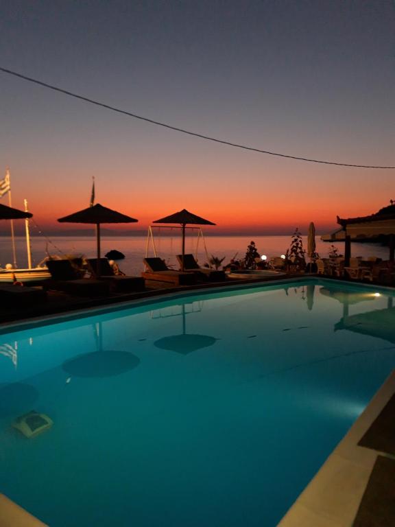 a swimming pool with a sunset in the background at Violetta Seaside Studios&Apartments in Karlovasi