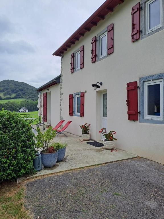 a white house with red shuttered windows and potted plants at location gite chez DENIS in Alçay-Alçabéhéty-Sunharette