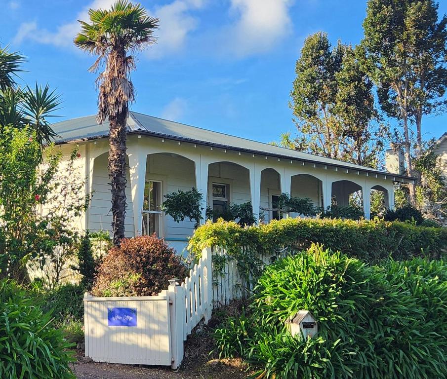 a white house with a palm tree and a fence at Wisteria Villa in Russell