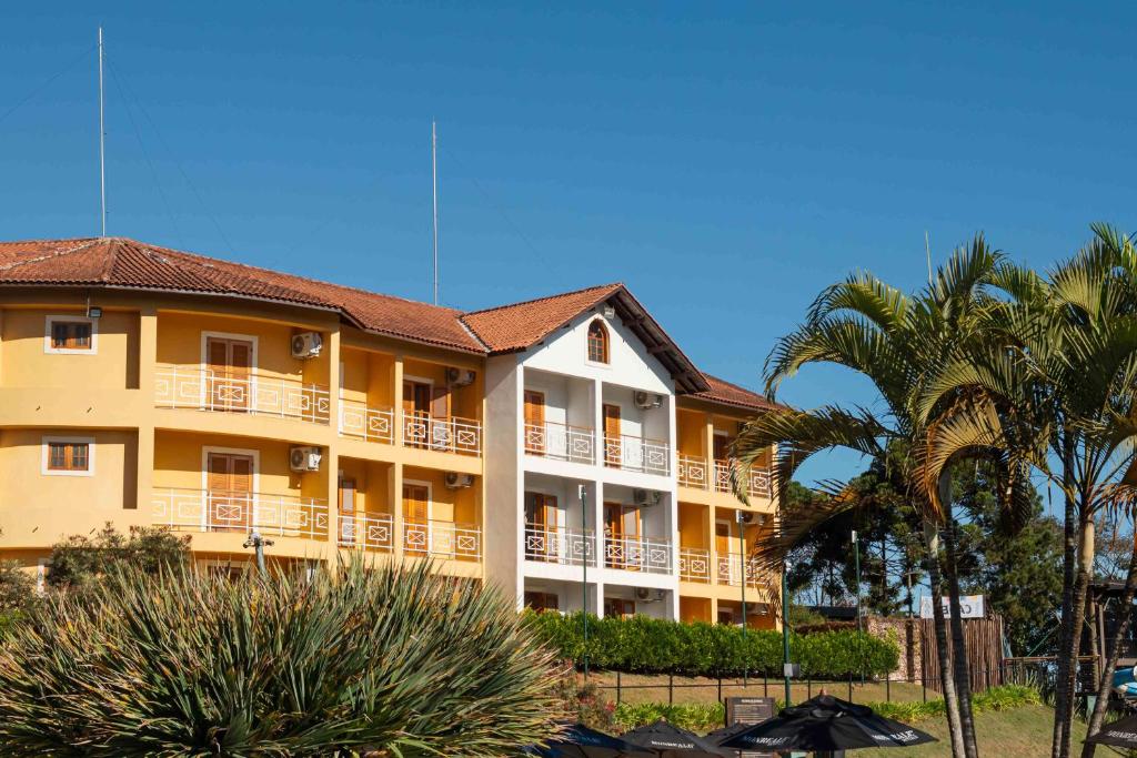 a large yellow building with palm trees in front of it at Hotel Monreale Resort in Poços de Caldas