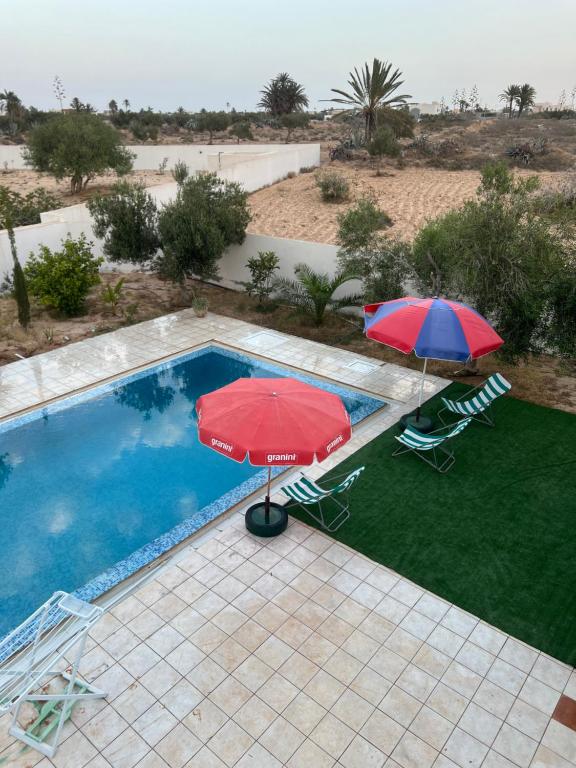 two umbrellas and chairs next to a swimming pool at Villa sedghiani in El Guecheïne