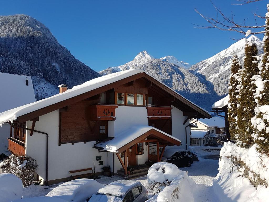 a house covered in snow with mountains in the background at Alpasella Ferienwohnungen in Sankt Gallenkirch