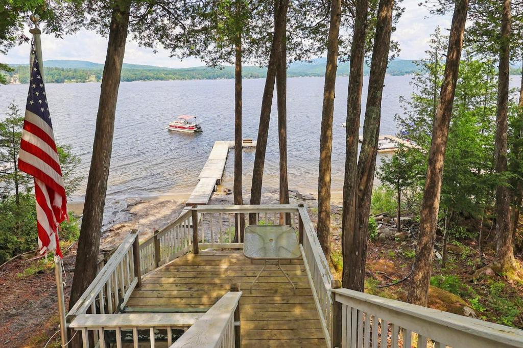 a dock with a boat on the water and an american flag at Waterfront Deck + Views: Schroon Lake Sanctuary in Schroon Lake