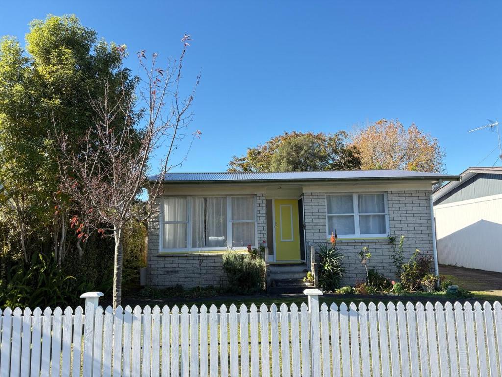 a white fence in front of a house with a yellow door at Cute Chartwell Cottage in Hamilton