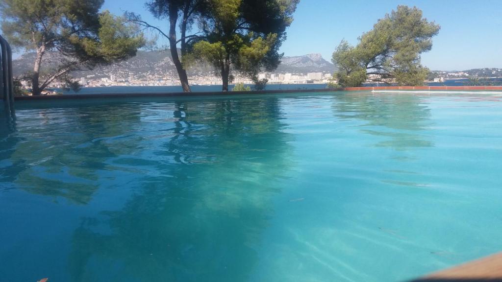 a pool of blue water with trees in the background at Villa-Chateau Les Terrasses, Tamaris, vues mer exceptionnelles au calme, plage en bas du domaine in La Seyne-sur-Mer