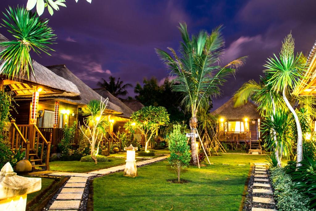 un complejo nocturno con palmeras y luces en Koji Garden Huts - CHSE Certified, en Nusa Lembongan