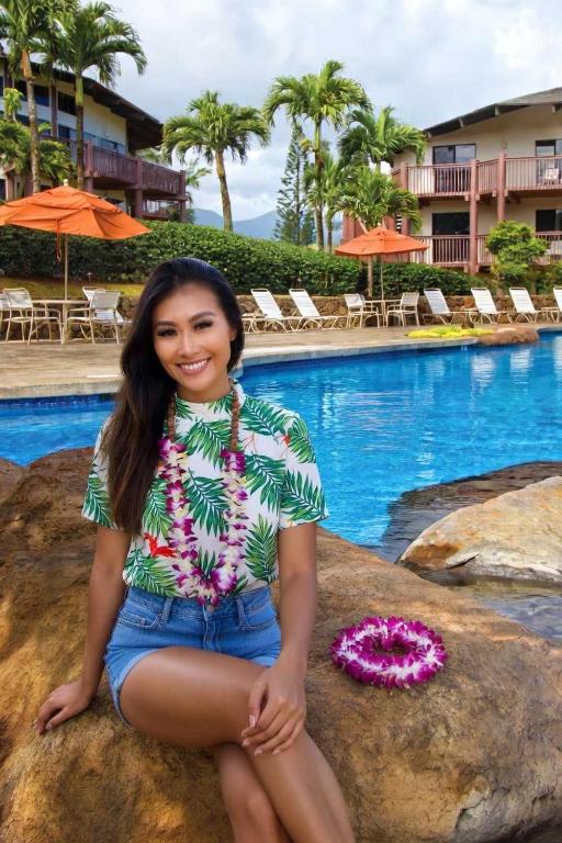 a woman sitting on a rock in front of a swimming pool at Ka Eo Kai Resort Studio Suite in Princeville
