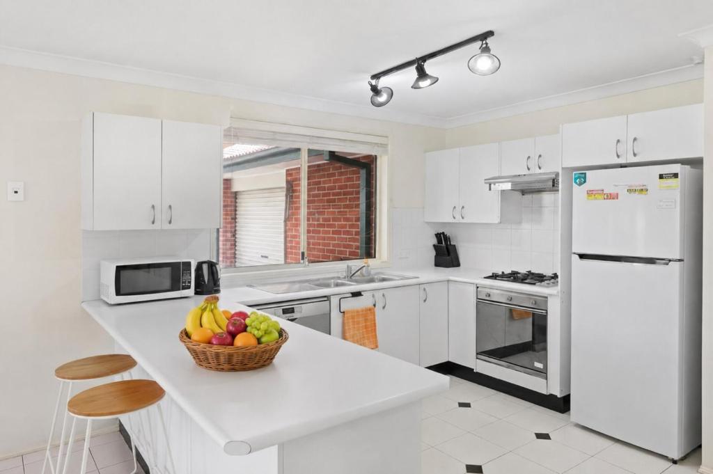 a white kitchen with a bowl of fruit on a counter at Escape from Relaxing Poolside House 3B in Narellan