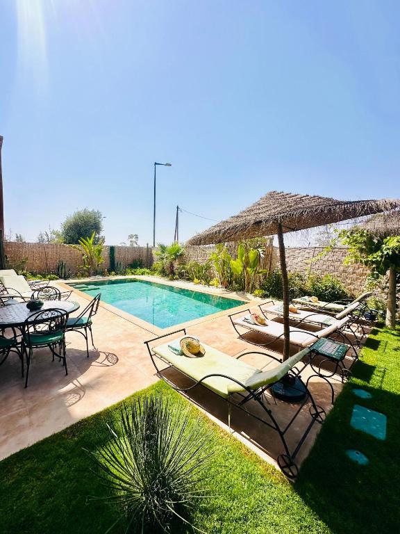 a swimming pool with lounge chairs and an umbrella and a table at Villa Dar Soka in Marrakesh