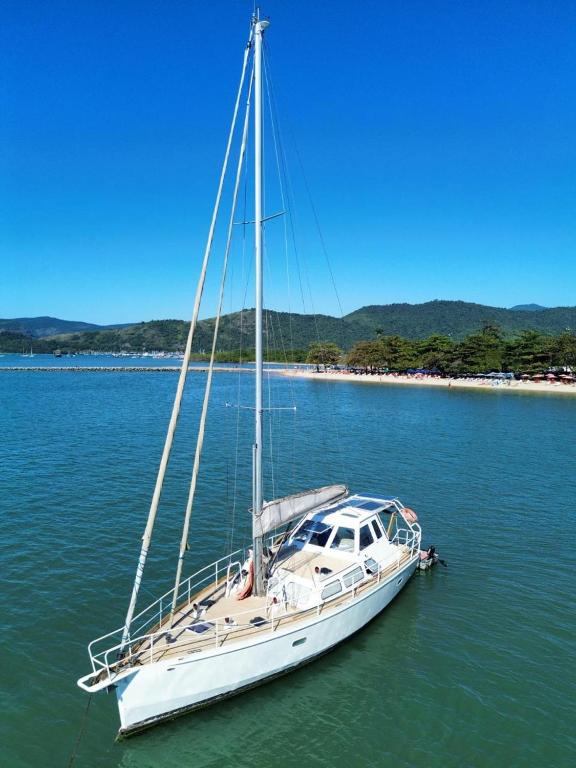 a sailboat docked in the water next to a beach at Passeio diurno e hospedagem de Veleiro Maverick in Paraty