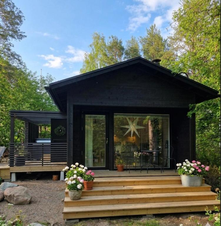 a black tiny house with a deck and flowers at Kataja Chalet with sauna and jacuzzi in Rovaniemi