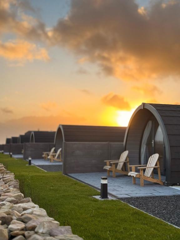 a group of chairs and a building with the sunset in the background at Bayview Glamping Pods Kerry in Ballyheigue