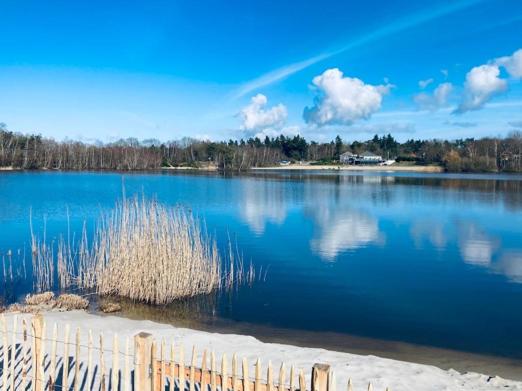 a large blue lake with a fence in front of it at Strandvilla met sauna in Westerhaar-Vriezenveensewijk