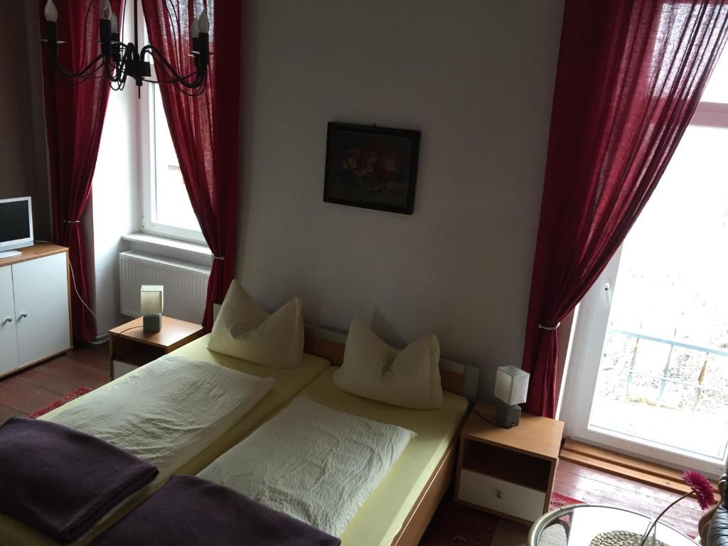 um quarto com uma cama e 2 janelas com cortinas vermelhas em Pension Gutshaus em Halle an der Saale