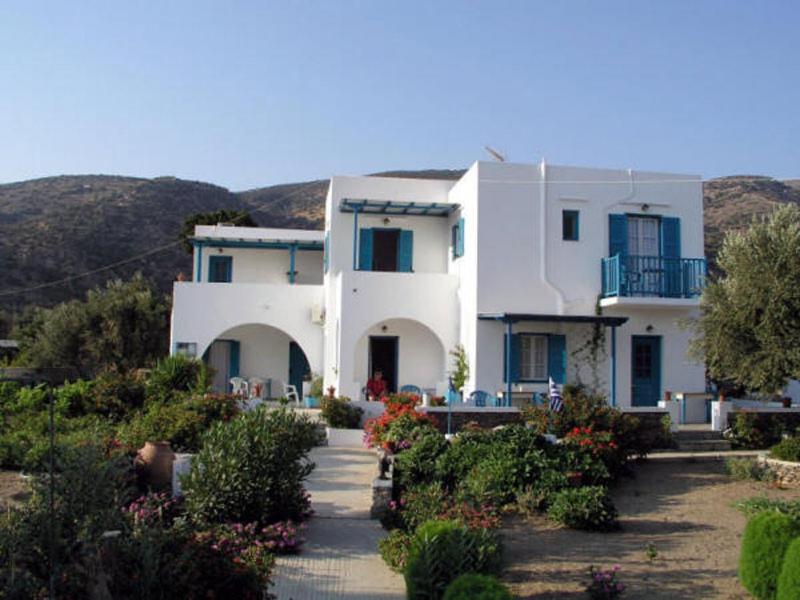 a large white house with blue windows and bushes at Areti studios in Vathi