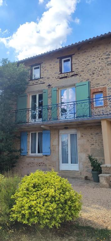 a brick building with green windows and a balcony at Gite de la vallée in Rochechouart
