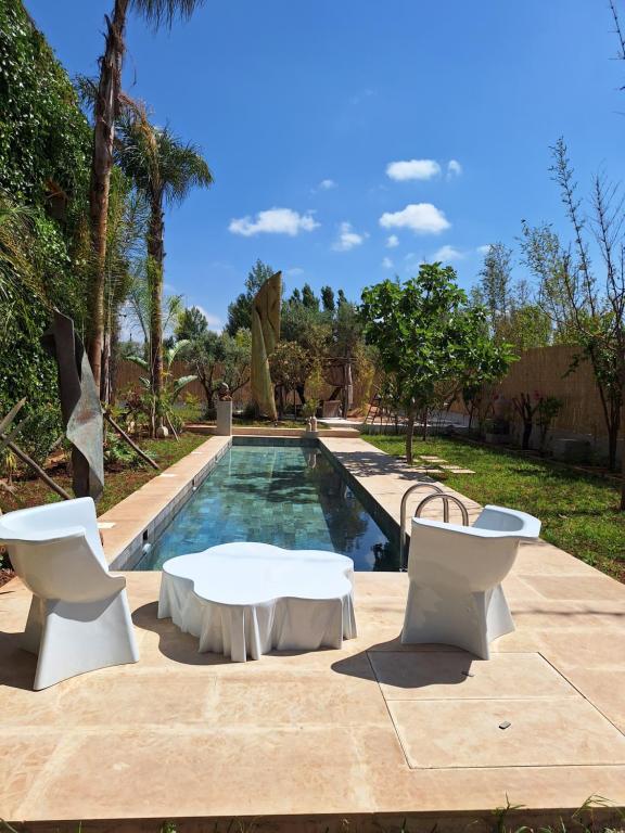 a swimming pool with two white chairs and a table and a table and a pool at La villa de mamie in Dar Ito Lahssene