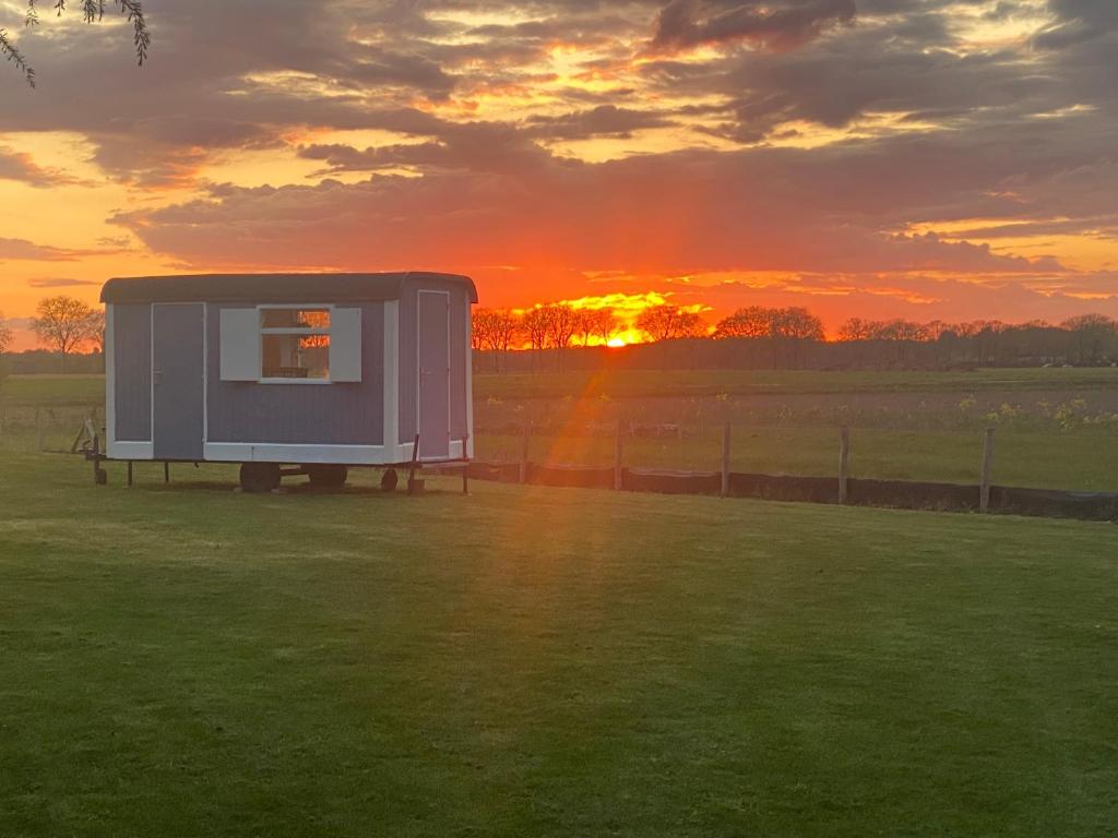 a trailer in a field with the sunset in the background at Sky Ballonvaarten & Accommodaties in Tilburg