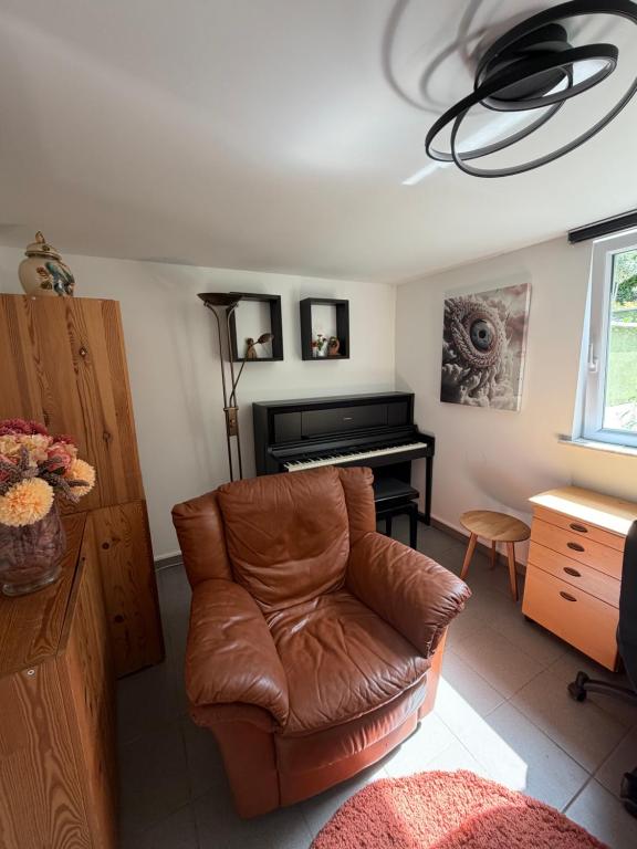 a living room with a leather chair and a piano at Cosy Studio naast station vlak bij Brussel in Hoeilaart