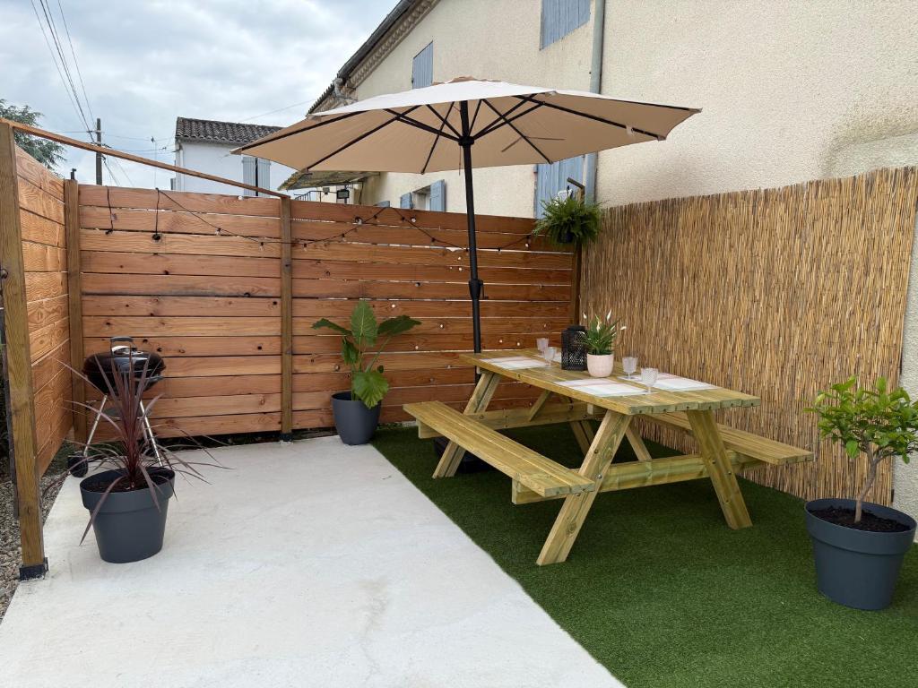 a wooden picnic table with an umbrella on a patio at Cosy Appartement avec Parking in Feugarolles
