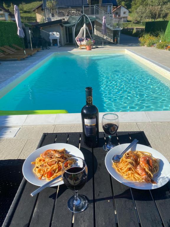 two plates of pasta and wine glasses on a table near a swimming pool at Dutaka Boutique Villa with Pool in Polje Ostružnica