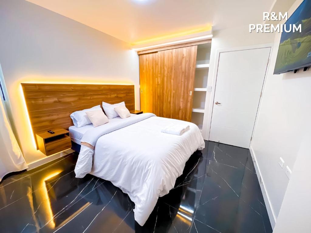 a bedroom with a white bed with a wooden headboard at Hospedaje R&M in Pelileo