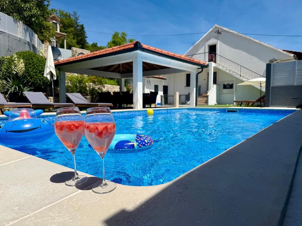 two wine glasses sitting next to a swimming pool at Kameni dvori - Family Villa with Pool & Jacuzzi for 8 in Imotski