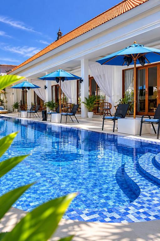 a swimming pool with blue umbrellas and chairs at Santai Suites Nusa Dua in Nusa Dua