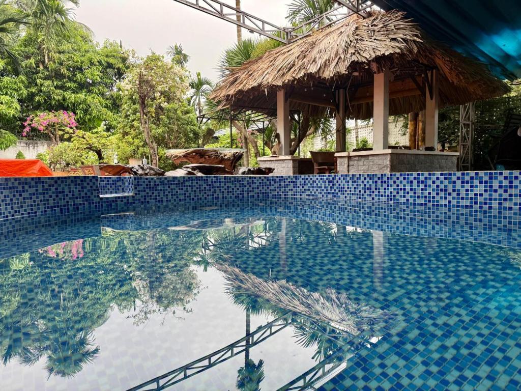 a swimming pool with a blue tile wall and a thatch hut at Cactos Pool & Palms Local Stay in Ho Chi Minh City