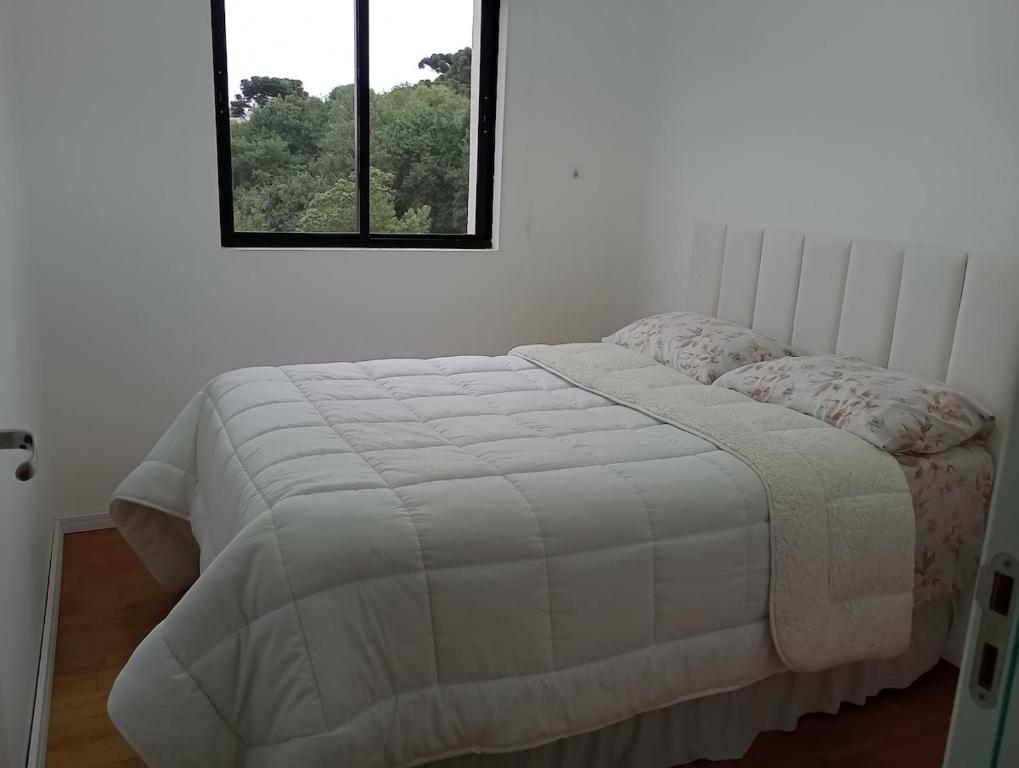a bedroom with a white bed with a window at Apartamento próximo ao Aeroporto e Curitiba in São José dos Pinhais