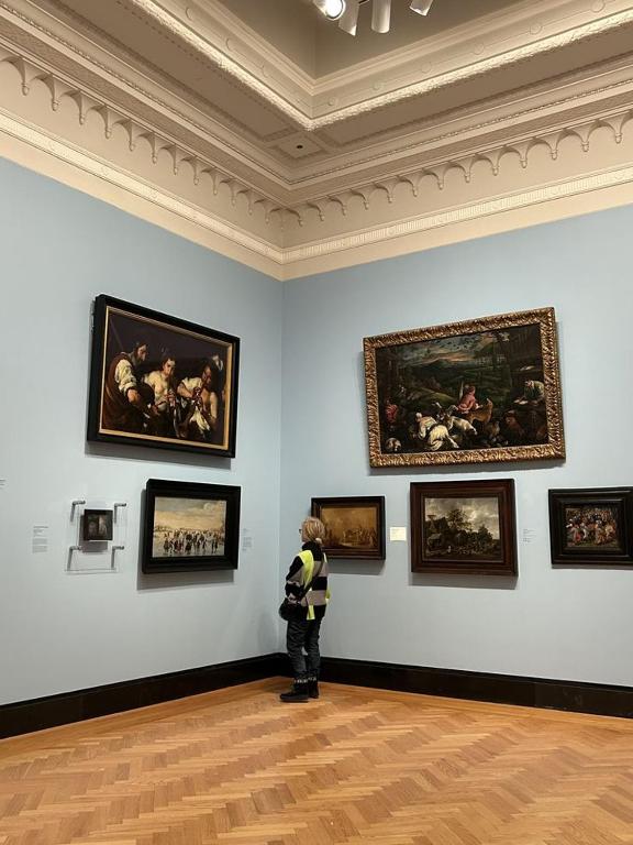 a person standing in an art museum looking at paintings at himalayan hotel in Jogīkuti