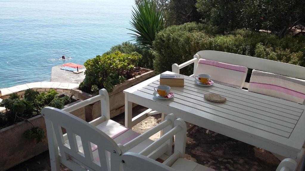 a white bench sitting next to a table and the water at Apartments Kvesic in Prizba