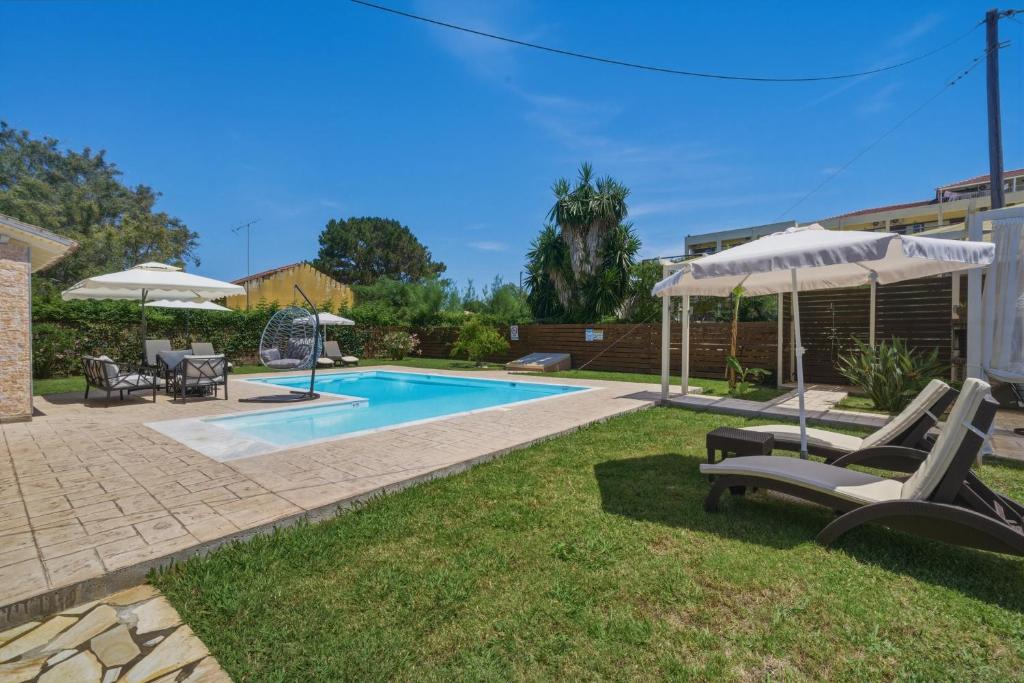 a backyard with a pool with chairs and an umbrella at Villa Astron in Agios Georgios
