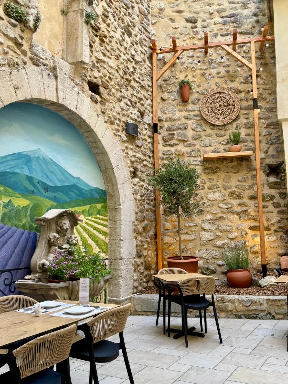 a patio with tables and chairs and a wall with a mural at Hotel Du Midi in Visan