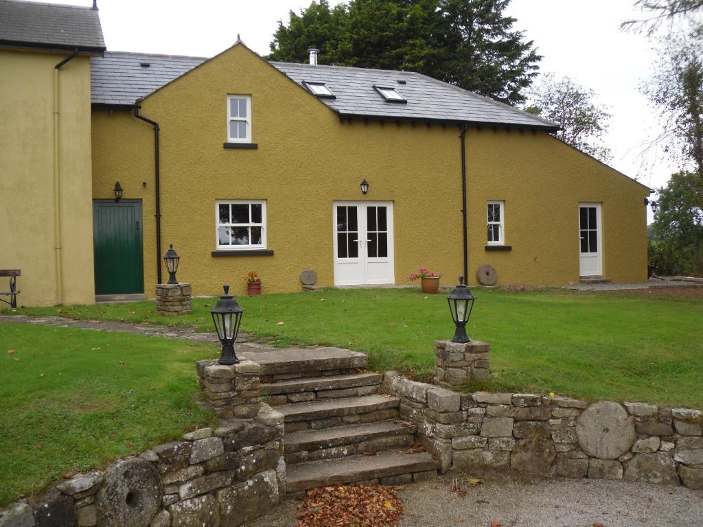 uma casa amarela com uma parede de pedra em frente a um quintal em The Homecoming Barn em Clogher