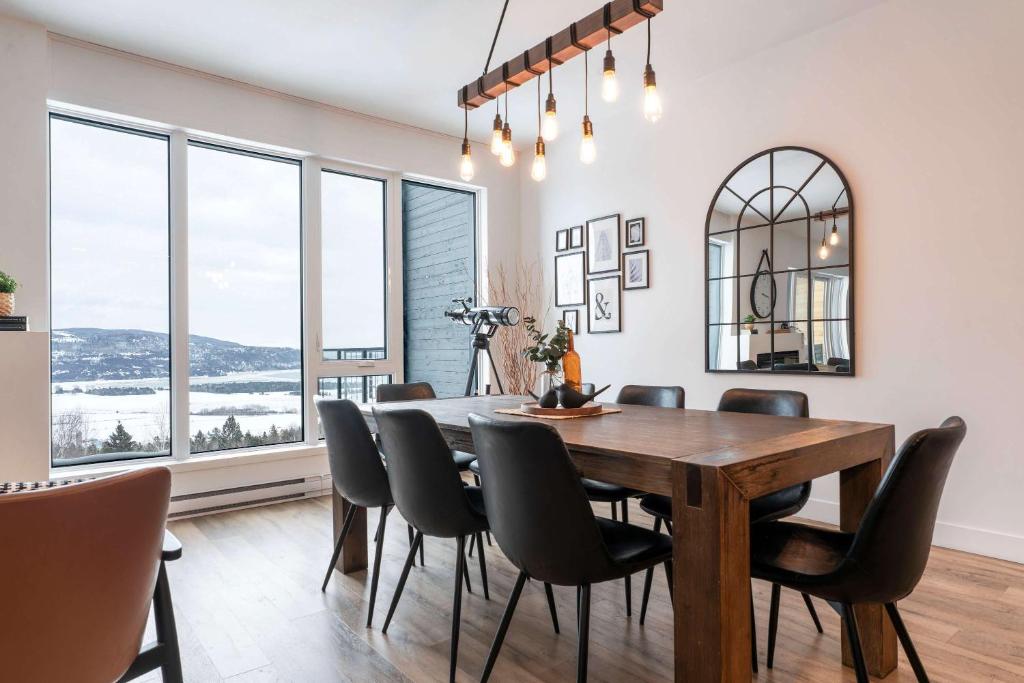 a dining room with a table and chairs and windows at 204 - Luxury Obsidian Condo - Elegance & Pool in Baie-Saint-Paul